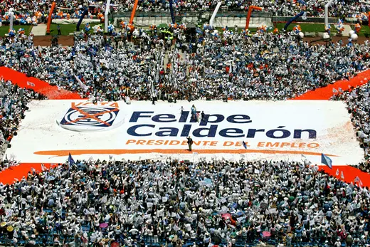 Large banner with writing saying "Felipe Calderón" is held up by crowd of supporters.