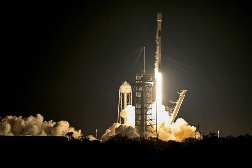 A rocket launches from a platform at night, creating a large plume of smoke on the ground.