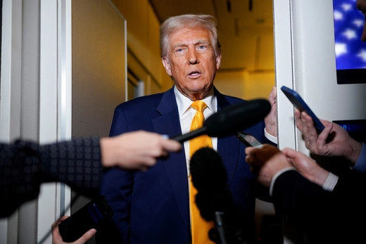 Trump stands in a doorway on Air Force One behind microphones held by reporters.